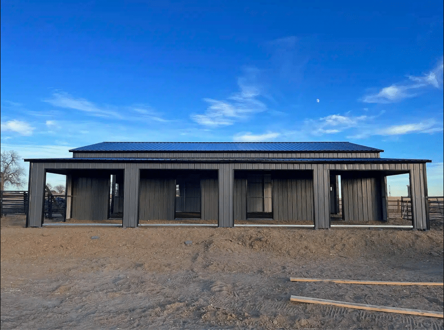 A metal barn with stalls with dirt around and blue sky